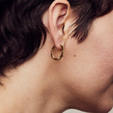 image of medium firework gold hoop earrings close up on ear on model with short brown hair