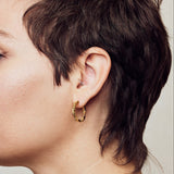 image of medium firework gold hoop earrings on model with short brown hair, headshot facing left