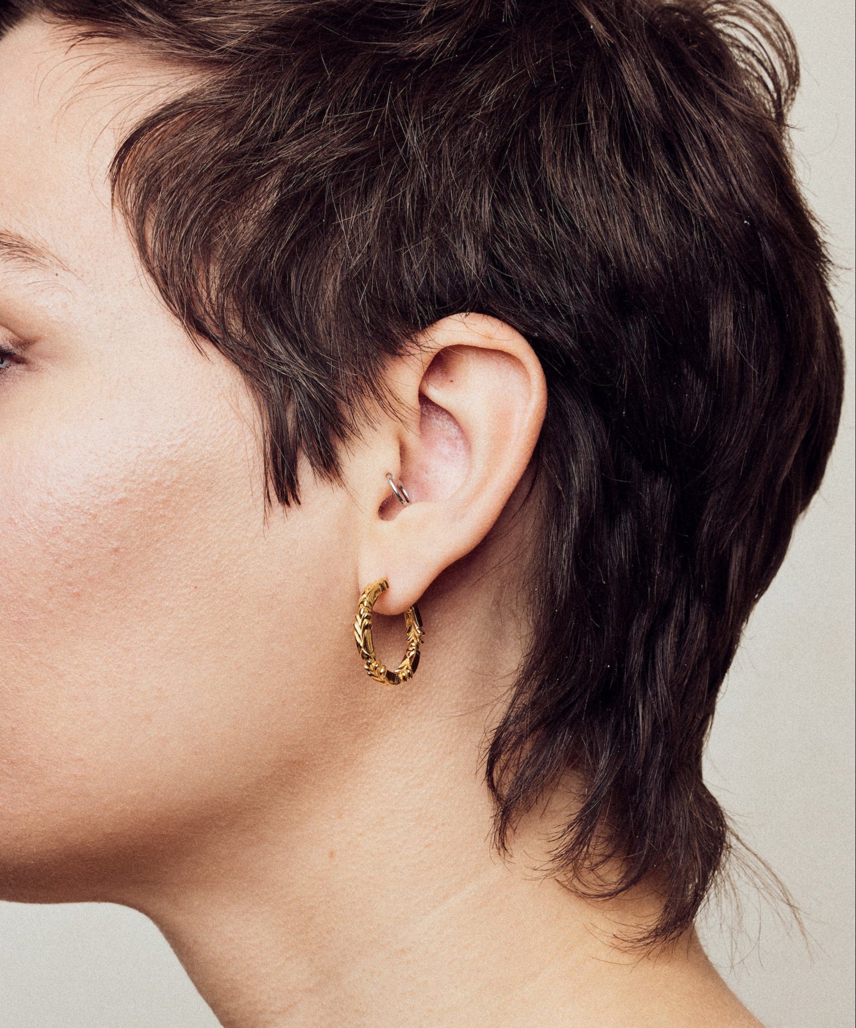 image of medium firework gold hoop earrings on model with short brown hair, headshot facing left
