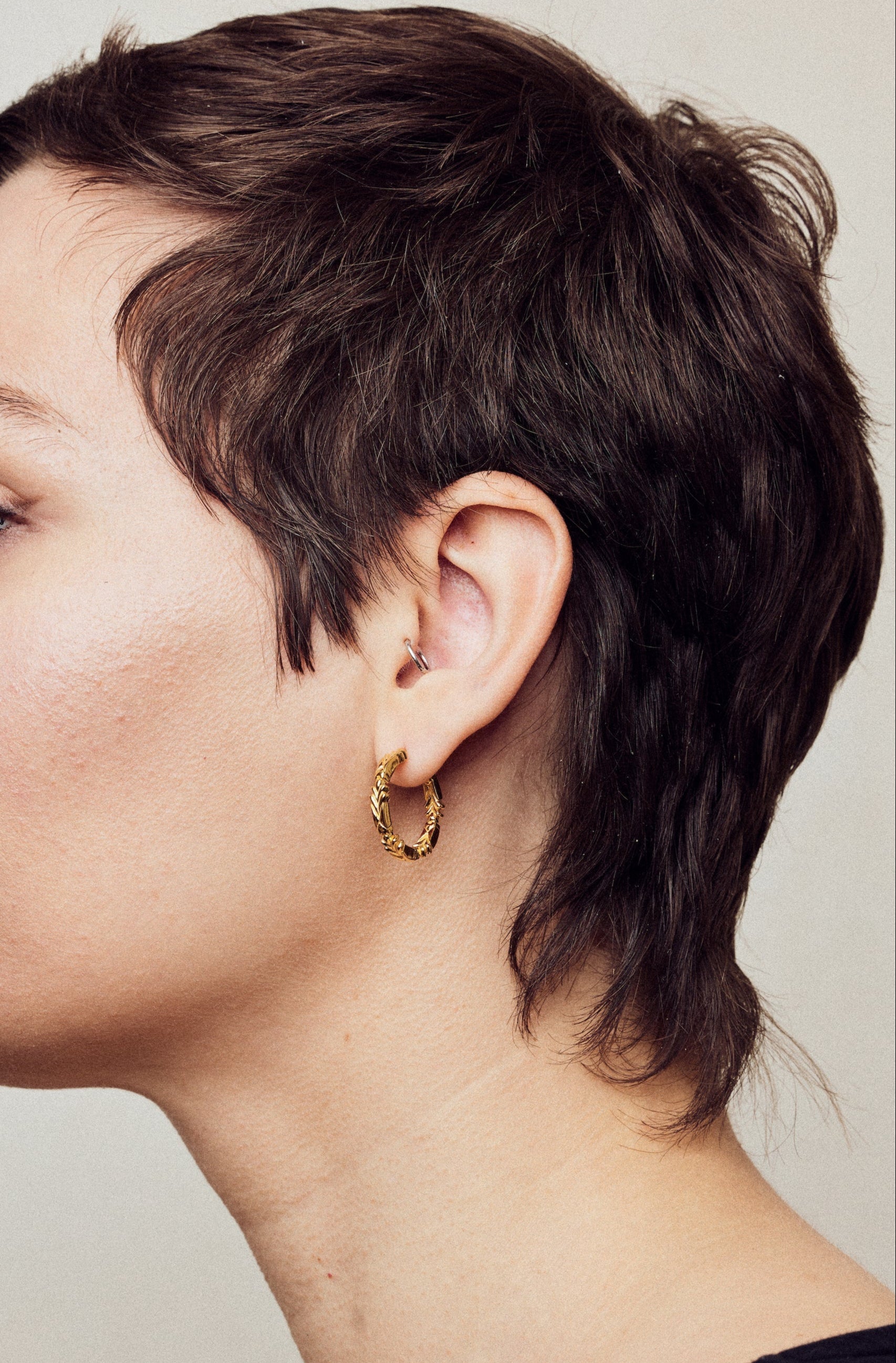 image of medium firework gold hoop earrings on model with short brown hair, headshot facing left