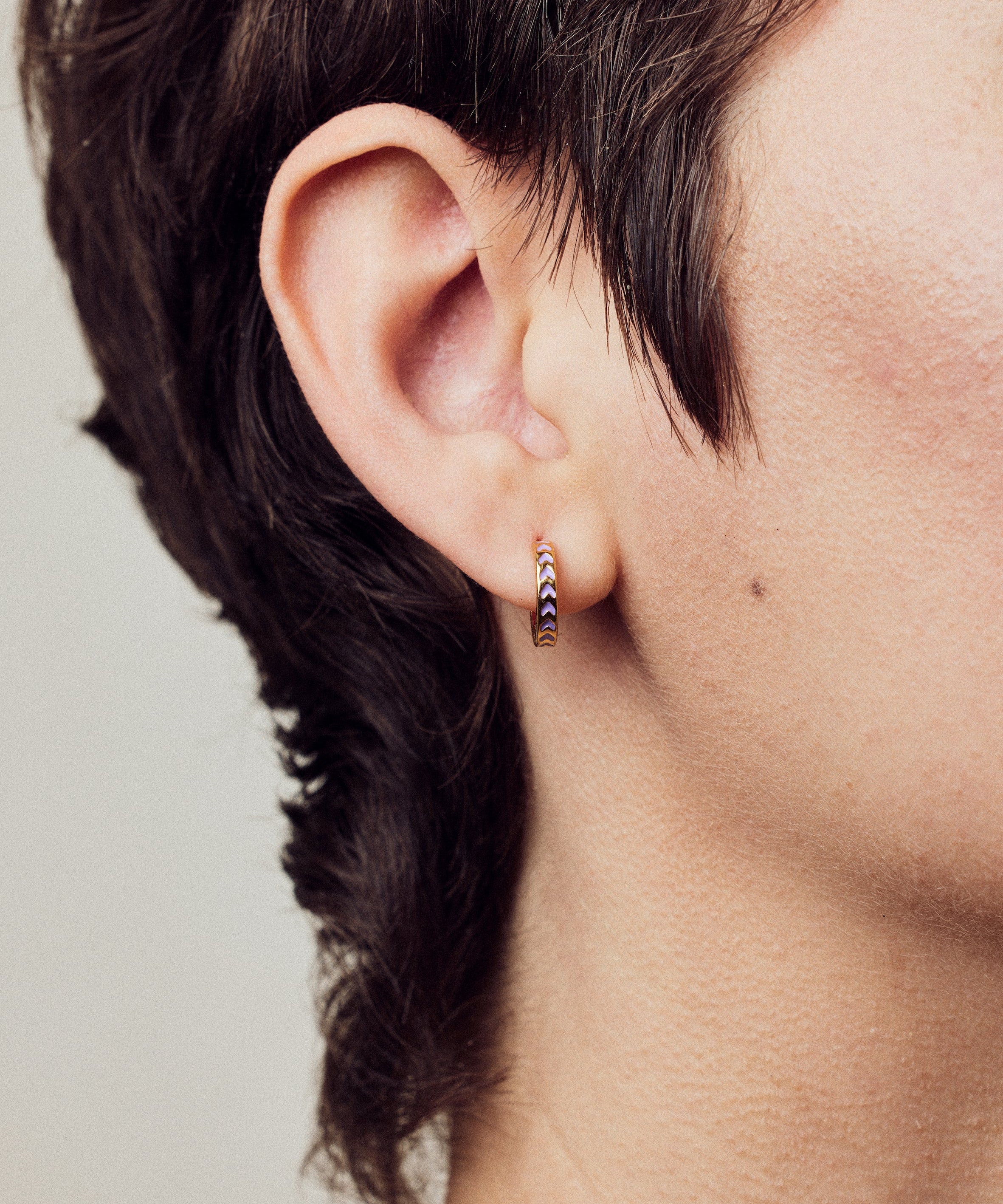 image of spark hoop enamel earrings in purple and gold shown close up on ear of model with white skin and short brown hair
