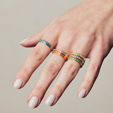image of spark enamel rings in six colours of enamel and gold on hand with white skin against a beige wall